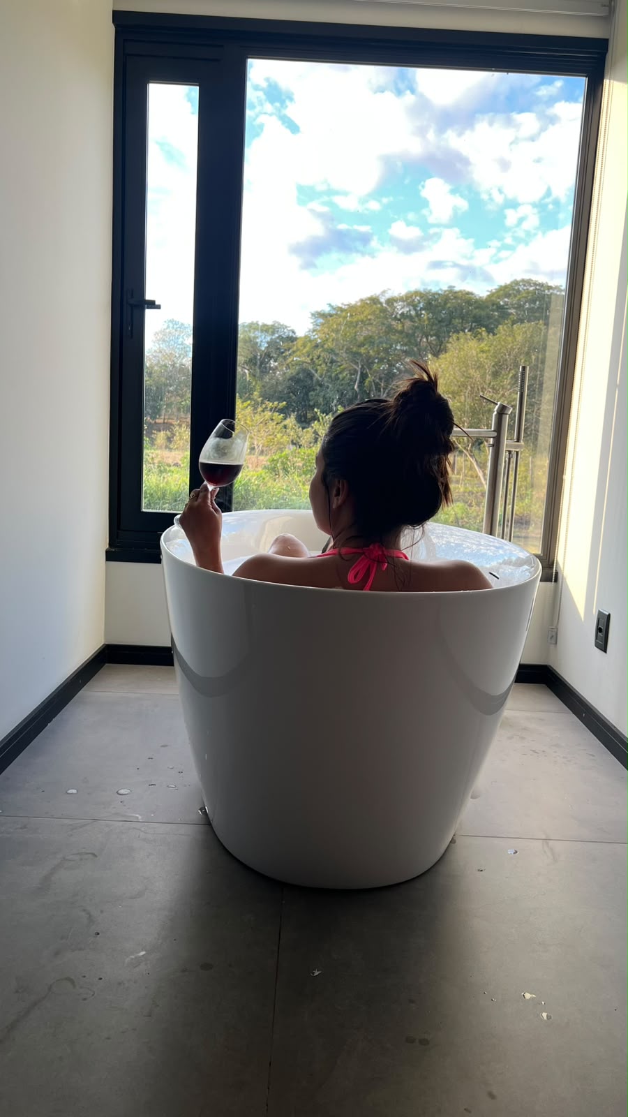 Banho na banheira com taça de vinho e vista para a mata